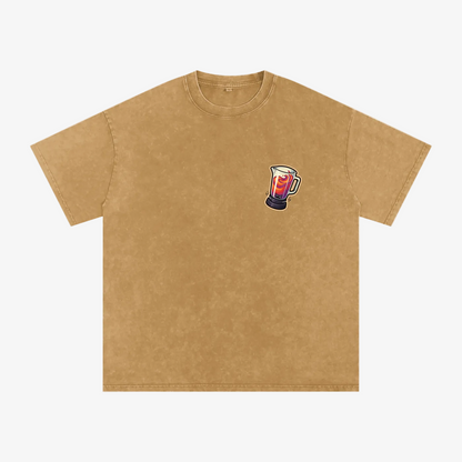 A tan short-sleeve crewneck t-shirt with a small graphic of a mug filled with red and white liquid on the left chest, displayed on a solid white background.