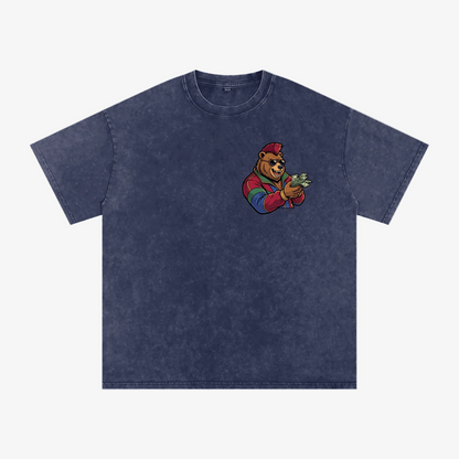 A dark blue acid-wash t-shirt featuring a cartoon graphic of a bear wearing a red cap and colorful striped sleeves, holding cash, on the left chest. The t-shirt is displayed flat against a solid white background.