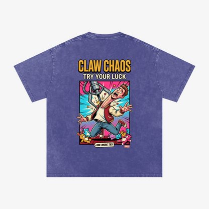 A purple mineral-wash t-shirt shown from the back, featuring a large colorful graphic print with the text 'CLAW CHAOS TRY YOUR LUCK' and a cartoon character.
