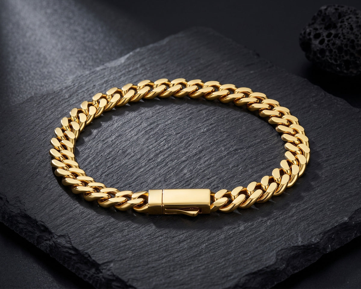 Gold 8mm curb chain bracelet with box clasp on a black slate slab beside a lava rock