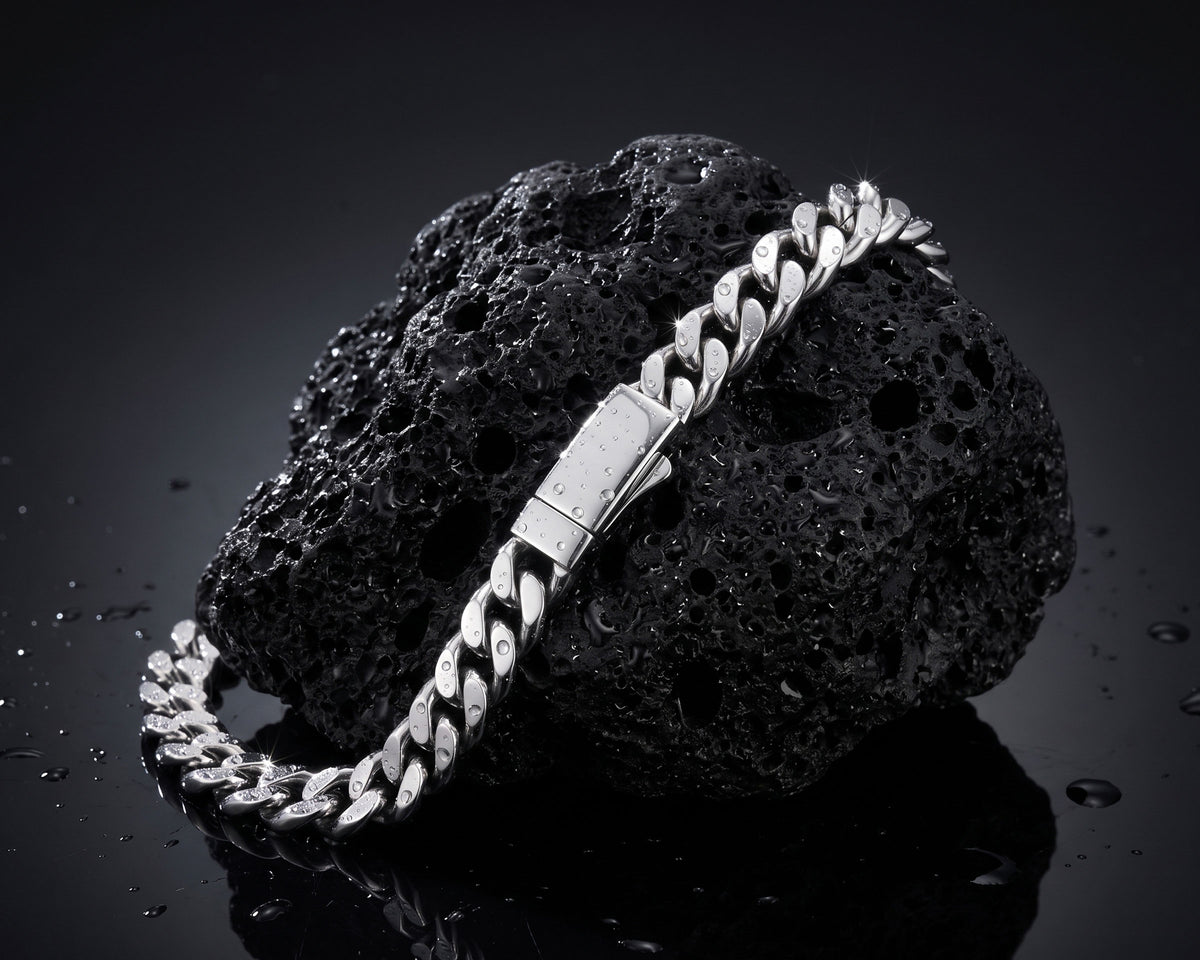 Silver 8mm curb chain bracelet draped over a black lava rock with water droplets