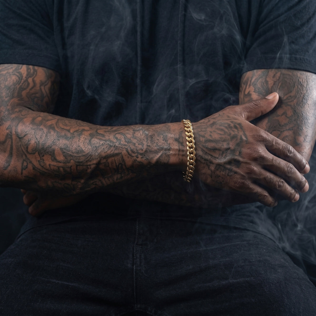 Man in a black t-shirt with tattooed arms crossed, wearing an 8mm gold curb chain bracelet