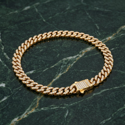 A gold-toned Cuban link chain bracelet, heavily embellished with clear pavé stones, displayed on a dark green marble surface.