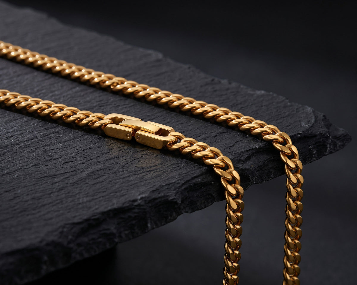 Section of a gold 5mm Miami Cuban chain with its clasp, flowing over the edge of black slate
