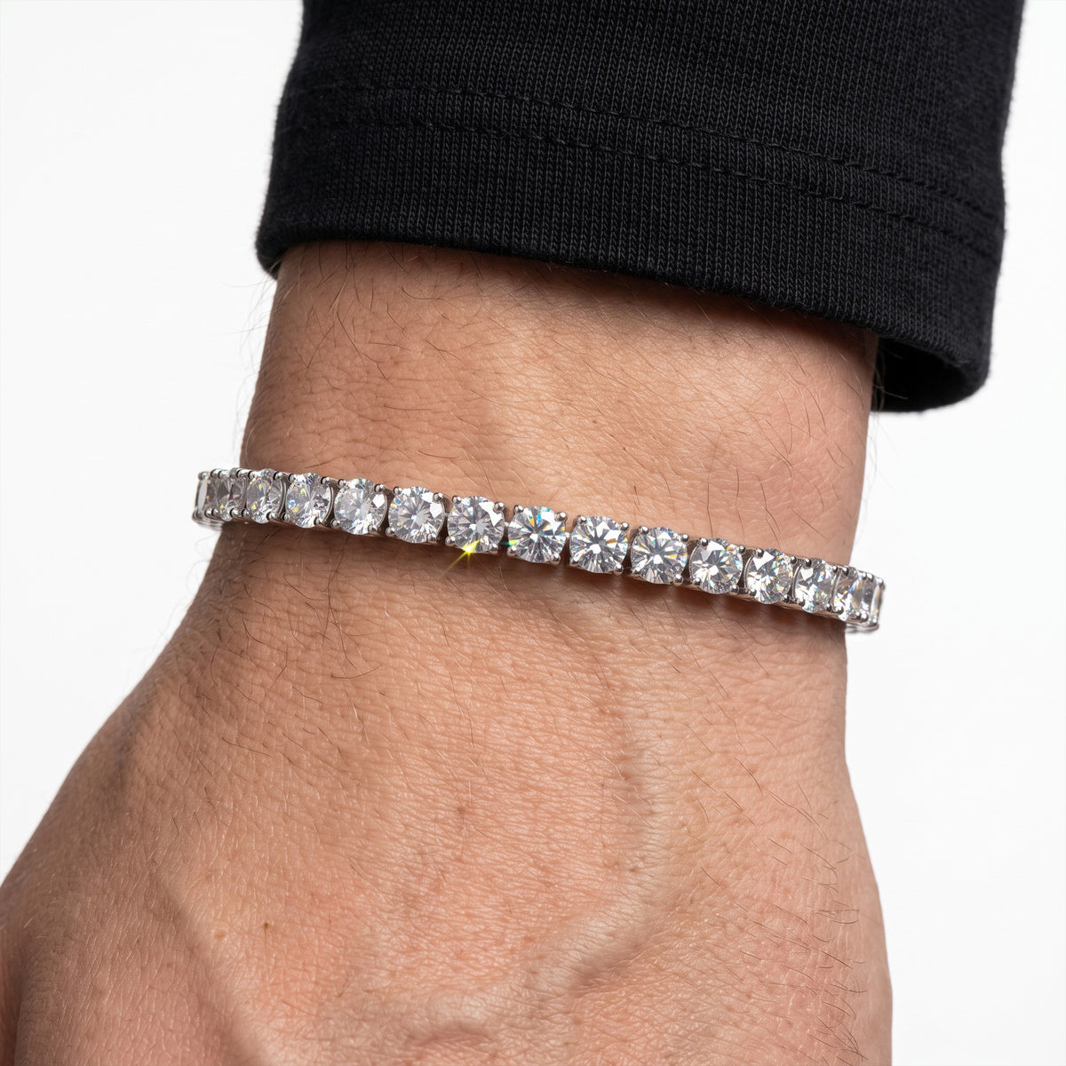 A close-up of a person's wrist wearing a silver tennis bracelet with round-cut clear gemstones, set against a plain white background.