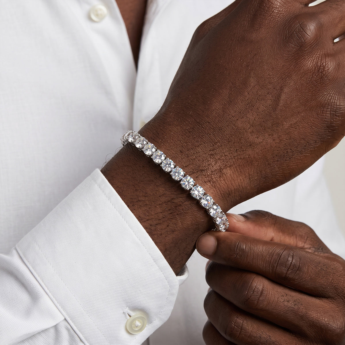 A close-up of a man's wrist wearing a silver tennis bracelet with clear round-cut stones, paired with a white dress shirt.