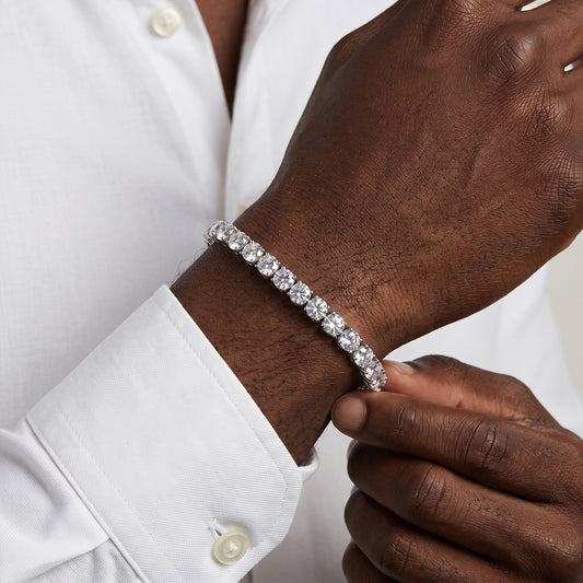 A close-up of a man's wrist wearing a silver tennis bracelet with clear round-cut stones, paired with a white dress shirt.