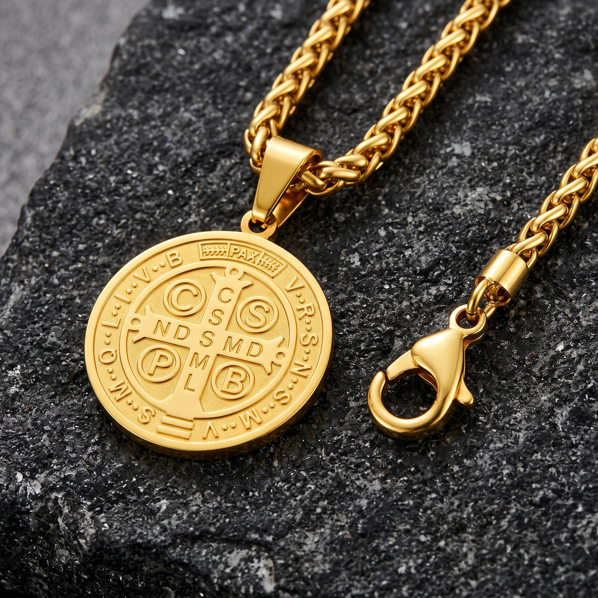 A gold-toned chain necklace with a round medallion pendant and a lobster clasp, displayed on a dark textured stone surface.