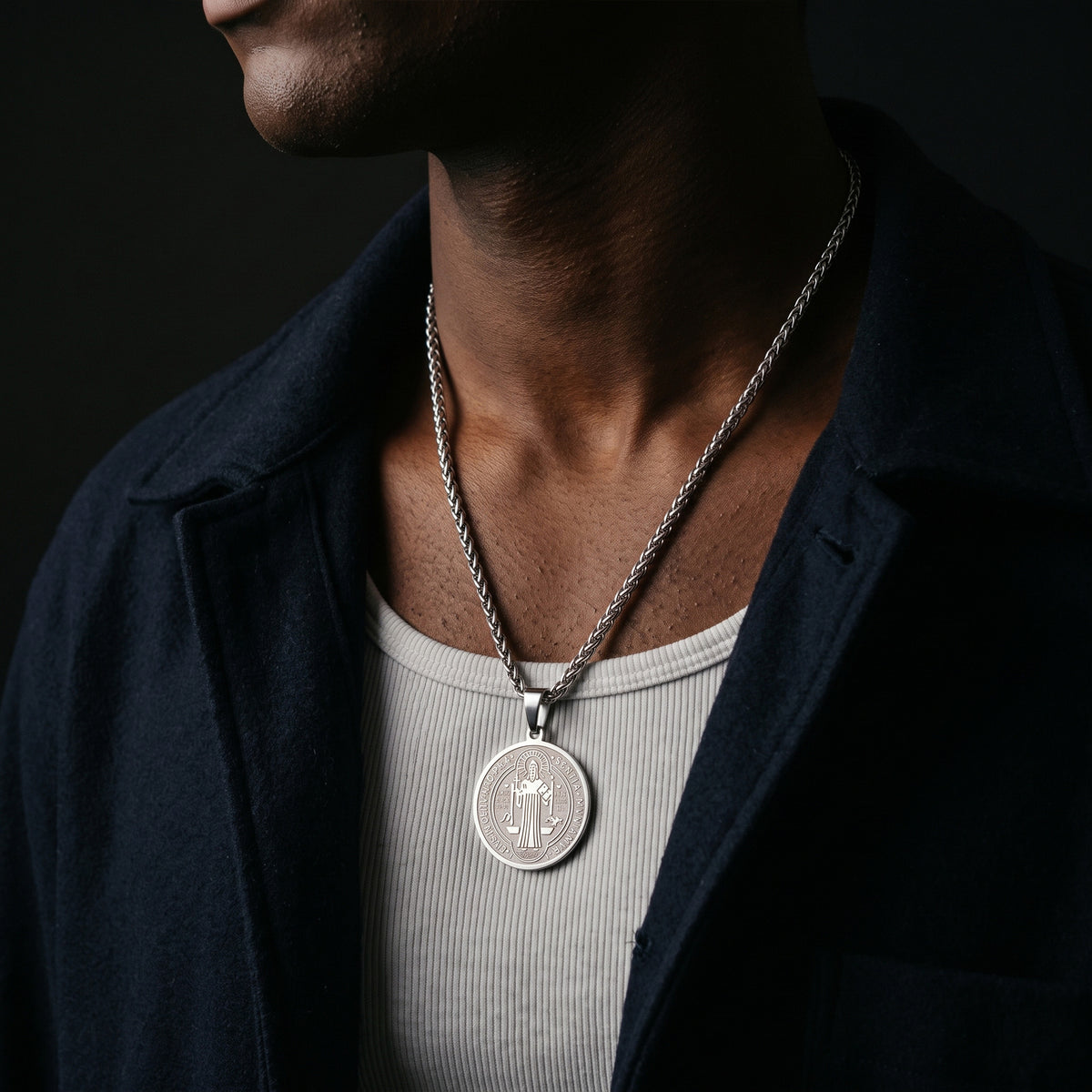 A close-up of a man wearing a silver pendant necklace with a cactus design, styled with a dark navy overshirt and a light gray ribbed t-shirt against a dark background.