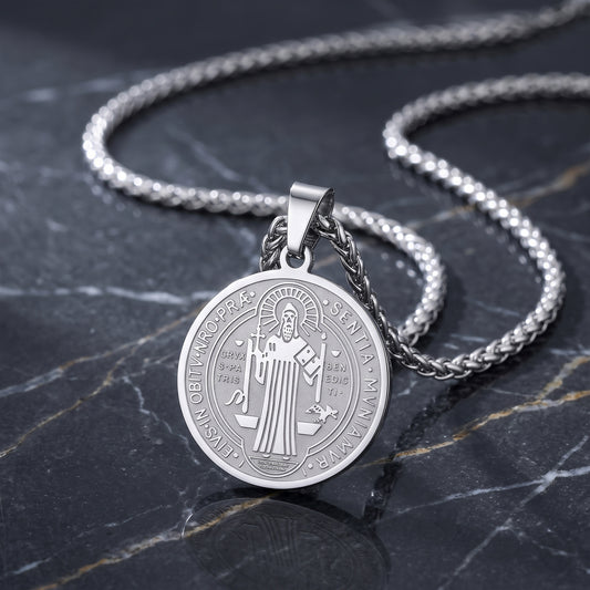 A silver round pendant necklace featuring an engraved religious figure, displayed on a dark marble surface with a matching silver chain.