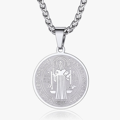 A silver-toned round pendant necklace featuring an engraved religious figure and text, suspended from a matching curb chain against a light gray background.