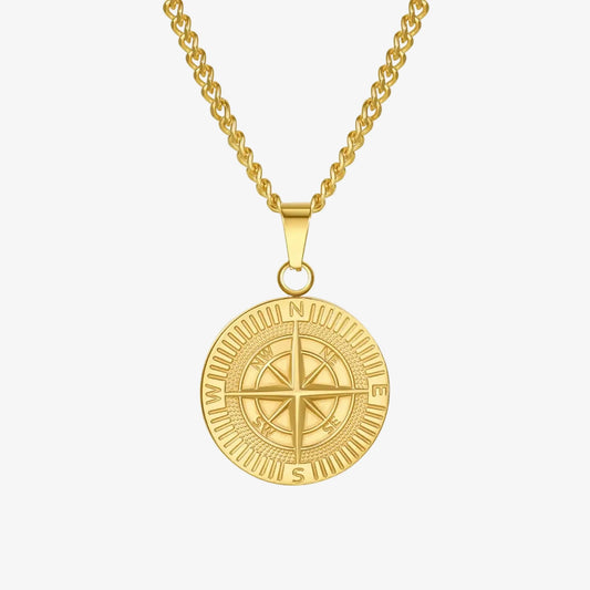 A gold-toned compass pendant necklace on a matching chain, shown against a clean white background with a subtle reflection below.