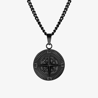 A black metal compass pendant necklace on a matching black chain, shown against a plain white background with a subtle reflection below.