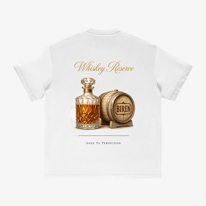 A white short-sleeve t-shirt shown from the back, featuring a graphic print of a whiskey decanter and a wooden barrel with 'BIREN' written on it. Above the illustration, the words 'Whiskey Reserve' are printed in a gold-colored script, and below, 'AGED TO PERFECTION' is printed in a thin black serif font.