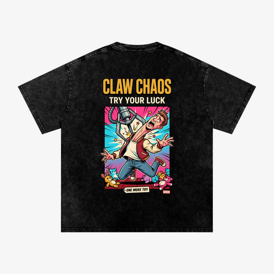 A black acid-wash graphic t-shirt shown from the back, featuring a colorful cartoon illustration of a man with a claw machine and the text 'CLAW CHAOS TRY YOUR LUCK' and 'ONE MORE TRY'.